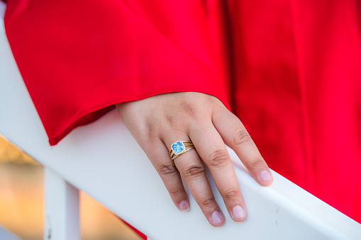 Female graduate wearing a silver class ring with a blue gemstone, and wearing a red graduation gown.