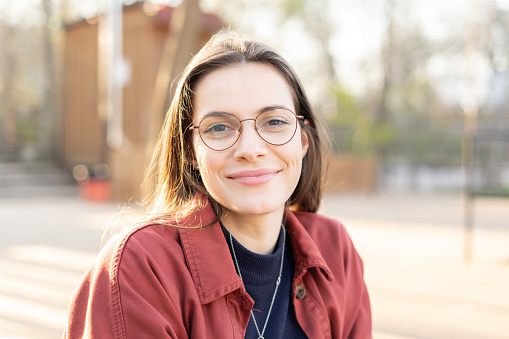 Head shot of a charming middle aged woman wearing eyeglasses looking in the camera with a slight smile outside during the sunset