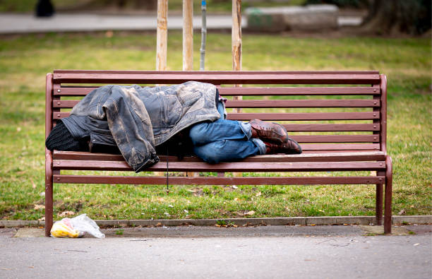 Homeless man sleeping on a bench Homeless man sleeps on a bench covered with his jacket in a public park during the day. homelessness stock pictures, royalty-free photos & images