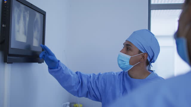 Mixed race male surgeon wearing protective clothing presenting x-ray on screen