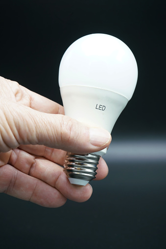 A man's hand holding LED light bulb. Close-up. Isolated on black.