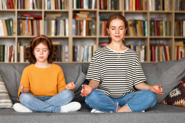 istock Peaceful mom and daughter meditating together while sitting in lotus pose on sofa at home 1315030407