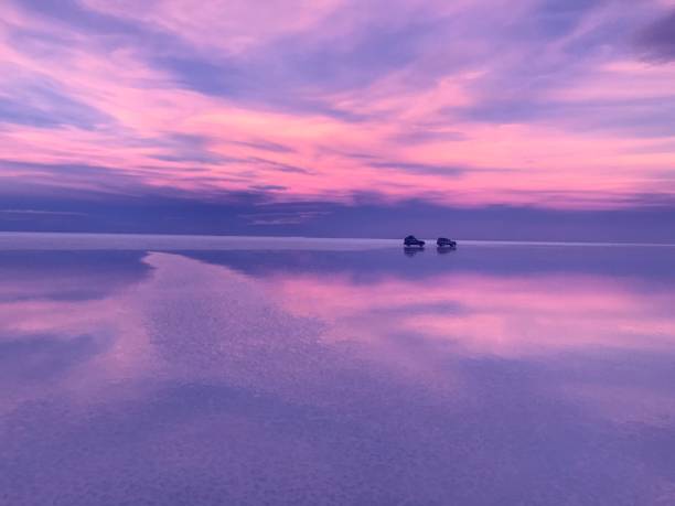 Purple pink sunset sky clouds reflection in sea water at mysterious night. Glowing heaven cloudscape over desert. Fantasy natural landscape. Cars on horizon. Surreal fantastic planet. Romantic sunrise Salt flat Salar de Uyuni salt flat stock pictures, royalty-free photos & images