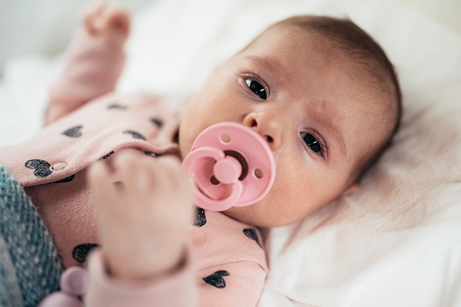 Baby girl with pacifier lying in her cot