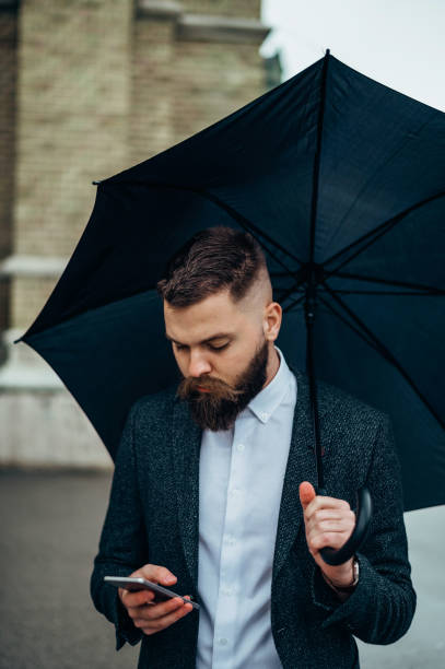 istock Young businessman using a smartphone and holding a black umbrella 1315042122