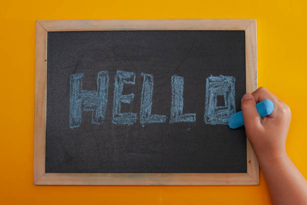istock girl's hand writing on a blackboard with blue chalk the word hello 1315045042