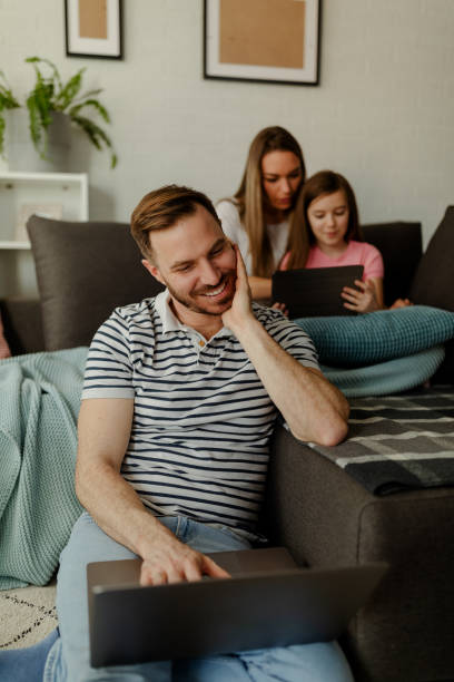 Father is sitting on the floor using laptop while mom and girl playing games. stock photo
