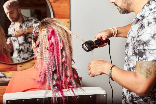 proffesional latin hairdresser making multicolor hairstyle to client using crimping irons. hairdressing services. young woman with colorful pink and blue dyed hair. - crimped imagens e fotografias de stock