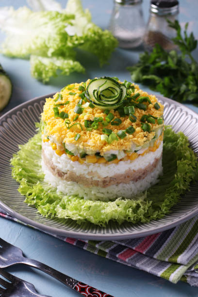istock Festive puff salad with cod liver, rice, eggs, corn and cucumber on a plate on light blue background. 1315053884