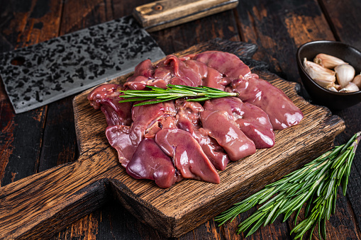 Raw liver chicken offals meat on a wooden cutting board with butcher cleaver. Dark wooden background. Top view.