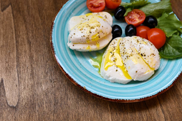 um prato com mussarela di búfalo em fatias com azeite e salada verde fresca, cerejas de tomate, azeitonas pretas. copie o texto espacial em um fundo de madeira. - mozzarella salad caprese salad olive oil - fotografias e filmes do acervo