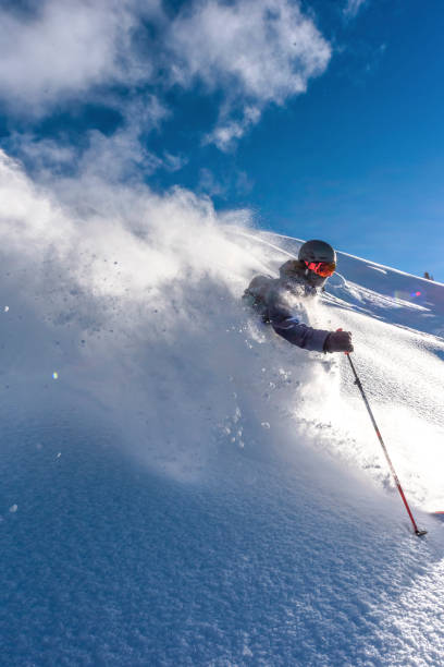 Skier descends steep mountain ridge through fresh powder snow Snow plume backlit extreme skiing stock pictures, royalty-free photos & images