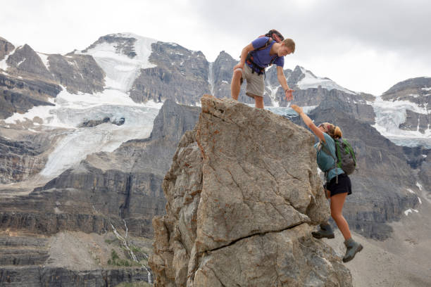 młody człowiek sięga po rękę rodzeństwa na szczyt góry - hiking young women outdoors t shirt zdjęcia i obrazy z banku zdjęć