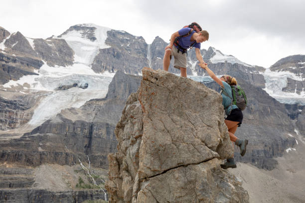 le jeune homme atteint pour la main de frère et sœur vers le haut du sommet de montagne - hiking young women outdoors t shirt photos et images de collection