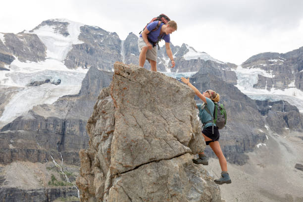 istock Young man reaches for sibling's hand up mountain peak 1315064005