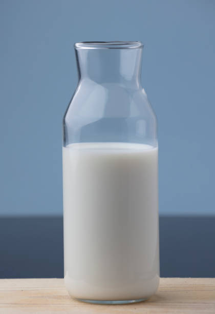 istock transparent glass milk bottle, on wood, blue background 1315070868