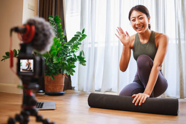 Asian woman yoga teacher filming yoga online class on video for Social media. Professional instructor in sportswear posing on VIDEO camera Asian woman yoga teacher filming yoga online class on video for Social media. Professional instructor in sportswear posing on VIDEO camera. Healthy lifestyle - technology at home. New normal lifestyle yoga instructor stock pictures, royalty-free photos & images