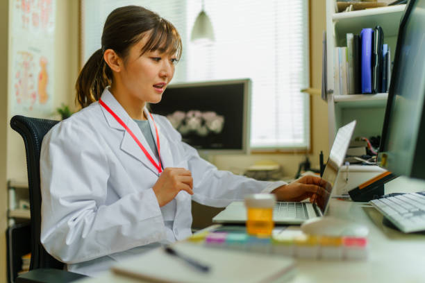 Female doctor having video call telemedicine meeting at her office A female doctor is having a video call telemedicine meeting at her office. japanese female doctor stock pictures, royalty-free photos & images