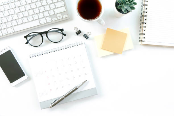 istock Modern white office desk table with computer, calendar, notebook, tree, glasses and cup of coffee. Top view with copy space, 1315113147