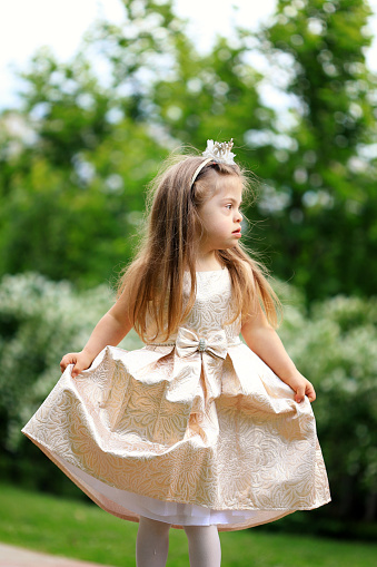 Cute girl in fairy dress and golden crown holding magic wand on pink background. Little princess