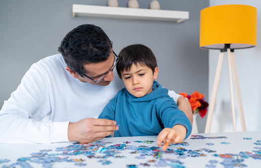 Little intelligent boy doing a jigsaw puzzle with his father. Leisure activity have fun at home