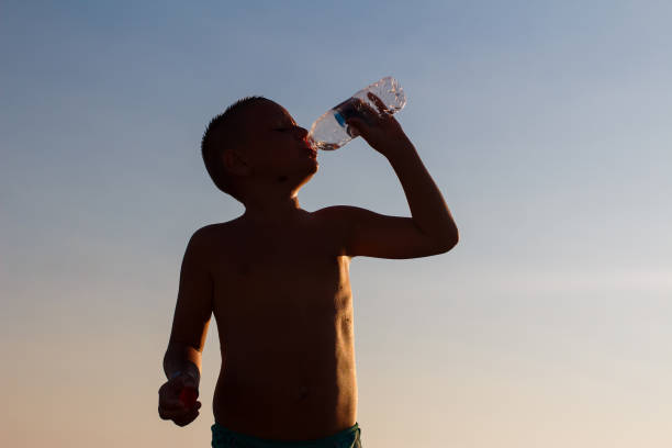 istock short-haired boy drinks water from a bottle in a counter light. silhouette 1315114337