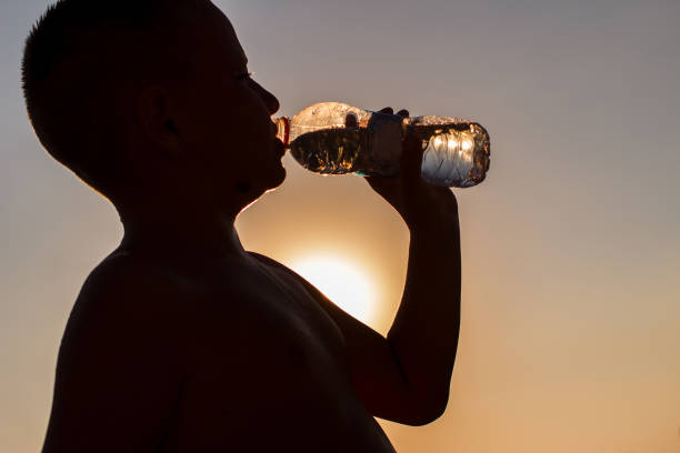 istock short-haired boy drinks water from a bottle in a counter light. silhouette 1315114342