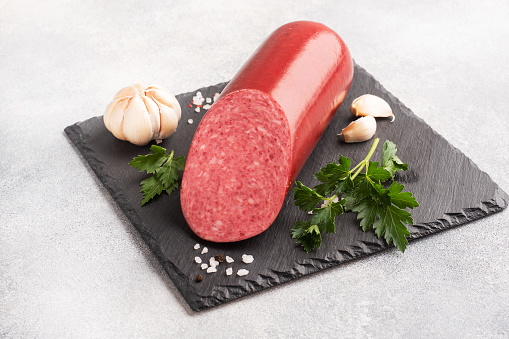 A loaf of salami Servelat sausage on a cutting Board with parsley and spices and garlic top view copy space