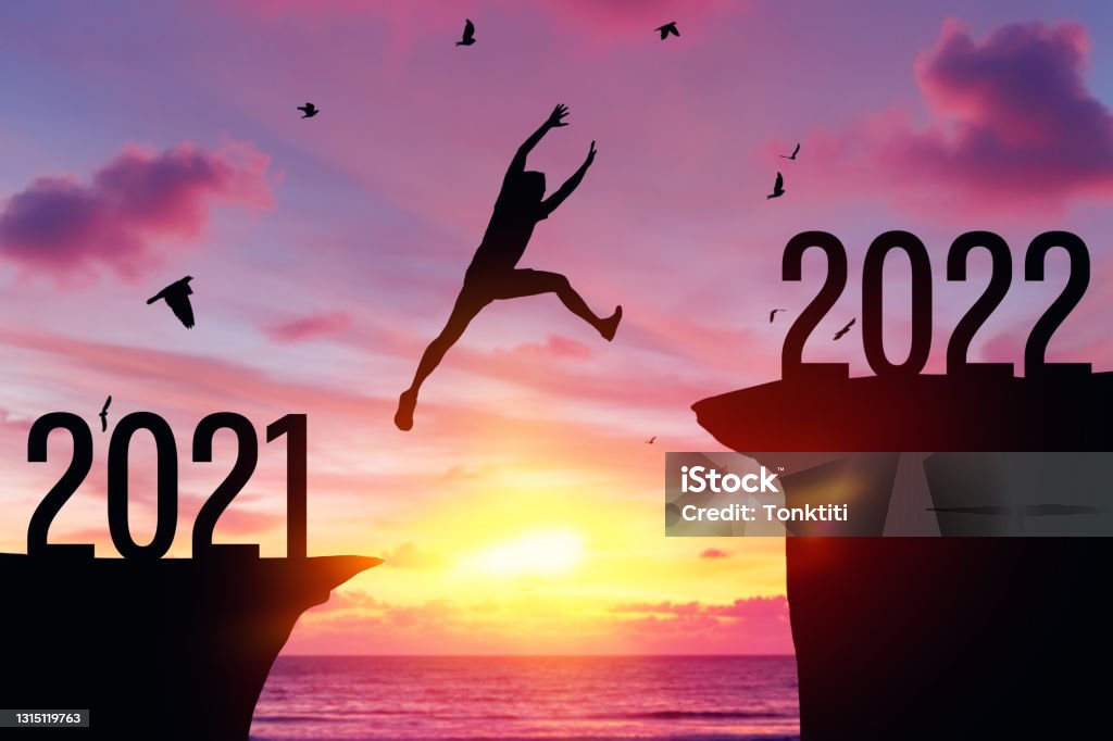 Silhouette man jumping between cliff with number 2021 to 2022 and birds flying at tropical sunset beach. Silhouette man jumping between cliff with number 2021 to 2022 and birds flying at tropical sunset beach. Freedom challenge and travel adventure holiday concept. Vintage tone filter effect color style. 2022 Stock Photo