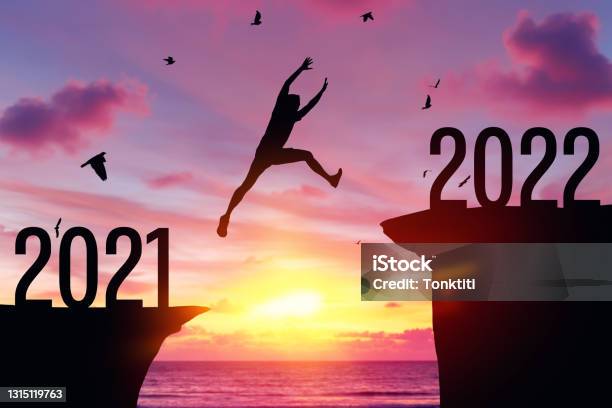 Silhouette Man Jumping Between Cliff With Number 2021 To 2022 And Birds Flying At Tropical Sunset Beach Stock Photo - Download Image Now