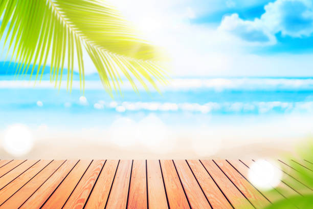 istock Blur tropical beach with bokeh sun light wave and palm tree on copy space empty old wood table abstract background. 1315119778
