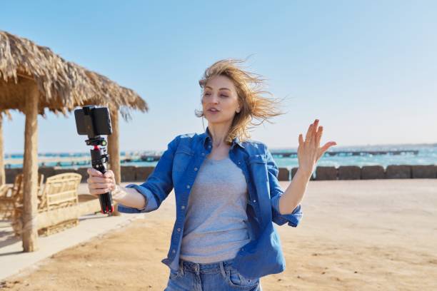 istock Middle aged woman looking at smartphone webcam talking recording video on sandy beach. 1315119815