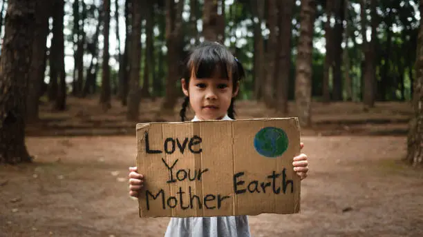 Photo of The little child girl with banners protesting over pollution and global warming in the forest to save planet earth. The concept of World Environment Day.