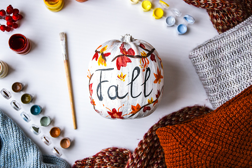 DIY. Do it yourself. Woman paints thanksgiving decorations on orange pumpkin for Halloween. Autumn harvest. Sweater home cozy. Paintbrush