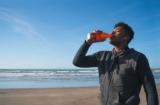 Portrait of an athletic man drinking something after training at the beach. Sport and health lifestyle.