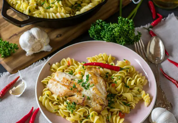 Pasta aglio e olio. Delicious and easy italien dish with garlic, olive oil, parsley and chili peppers served with fried fish fillet on kitchen table background from above