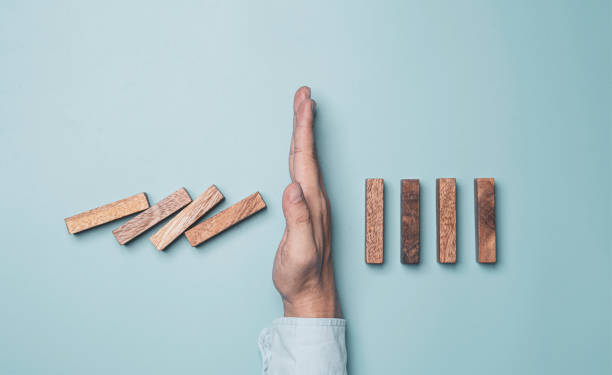 businessman hand protecting rectangle  block which falling to stop dominos others rectangle standing on blue background. risk and crisis management concept. - preventative imagens e fotografias de stock