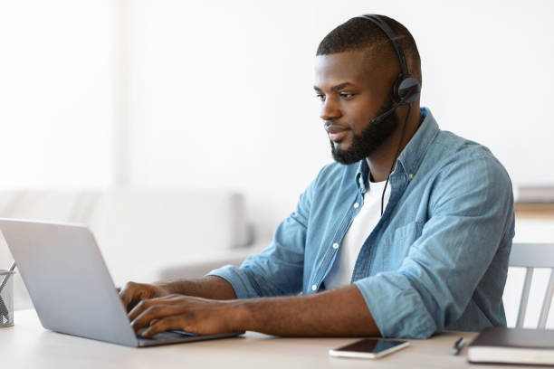 istock Black millennial man in headset working remotely with laptop at home office 1315129085