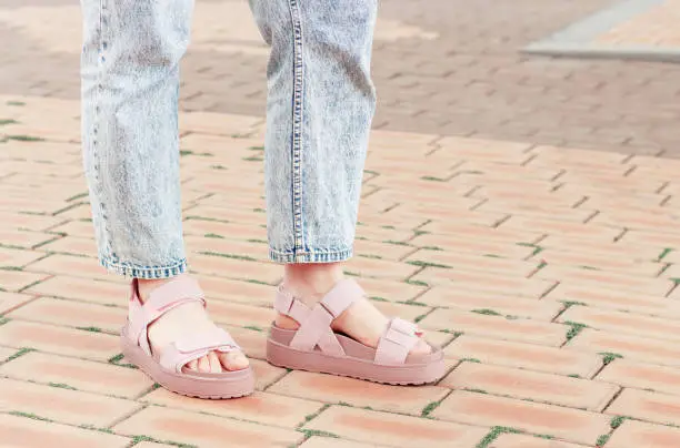 Photo of Female feet in pink sandals on concrete background close-up.