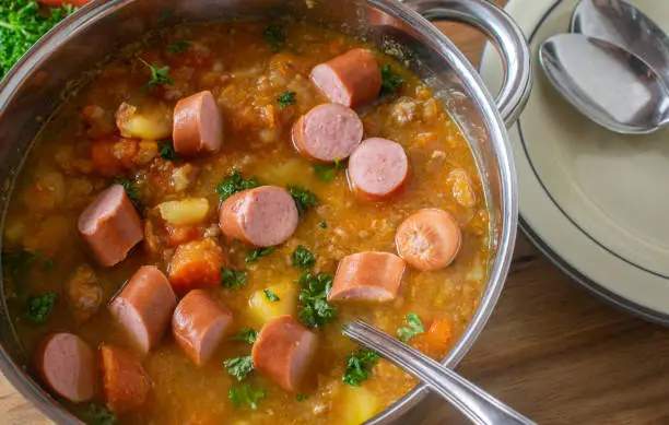 Delicious home cooked carrot stew with minced pork meat and boiled sausages served in a large pot on kitchen table background from above