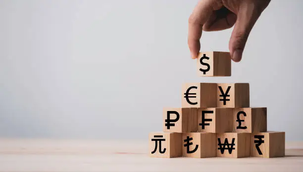 Photo of Hand putting wooden cube of US dollar sign to Renminbi Yuan  Yen Euro and Pound sterling sign.US dollar is main and popular currency of exchange in the world.Investment and saving concept.