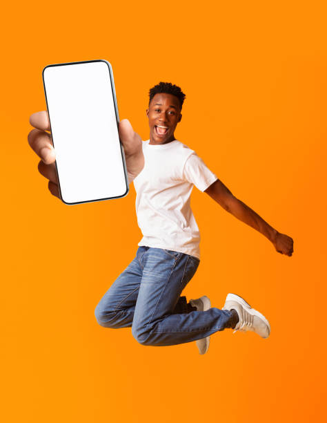 istock Overjoyed black man jumping and holding smartphone with white screen, mockup for advertisement or app design 1315134371