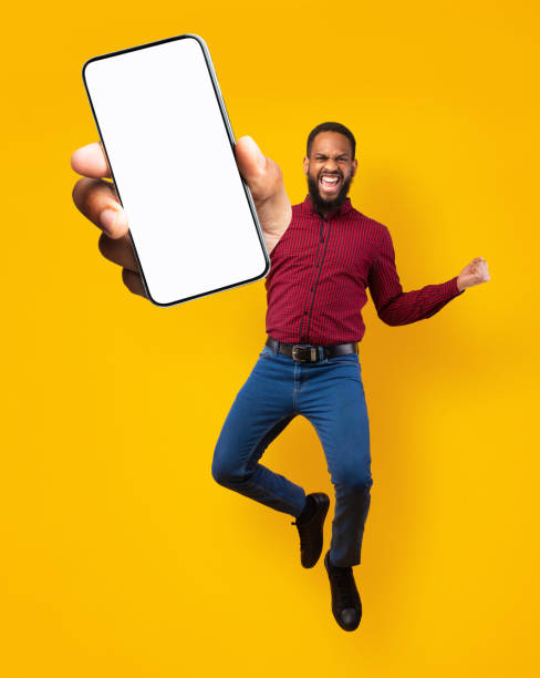 istock Black man jumping, gesturing YES and showing cellphone with empty space for mobile app on screen, orange background 1315135303