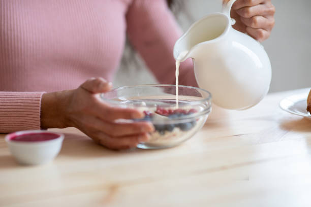 Unrecognizable Female Preparing Muesli With Fruits For Breakfast, Pouring Milk To Bowl