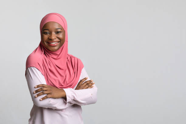 sonriente dama negra en hiyab posando en gris - islam fotografías e imágenes de stock