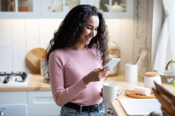 istock Mobile Communication. Young Beautiful Woman Using Smartphone And Drinking Coffee In Kitchen 1315136277
