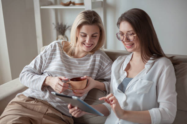 istock Two young women friends using tablet together, sitting on the co 1315136699