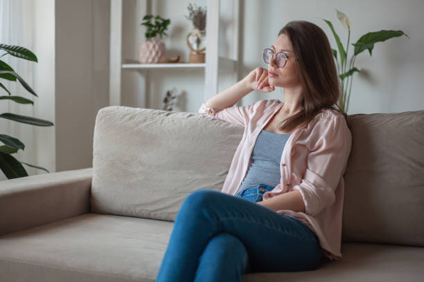 istock Young woman with eyeglasses sitting on sofa, looking the window 1315136787