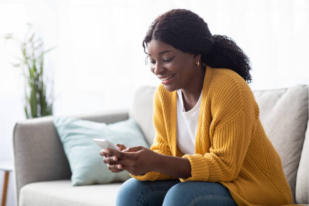 istock Smiling black lady sitting on couch, using smartphone 1315137019