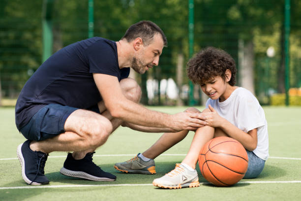 insegnante che aiuta ragazzo con un trauma al ginocchio dopo aver giocato a basket - athlete coach basketball male foto e immagini stock